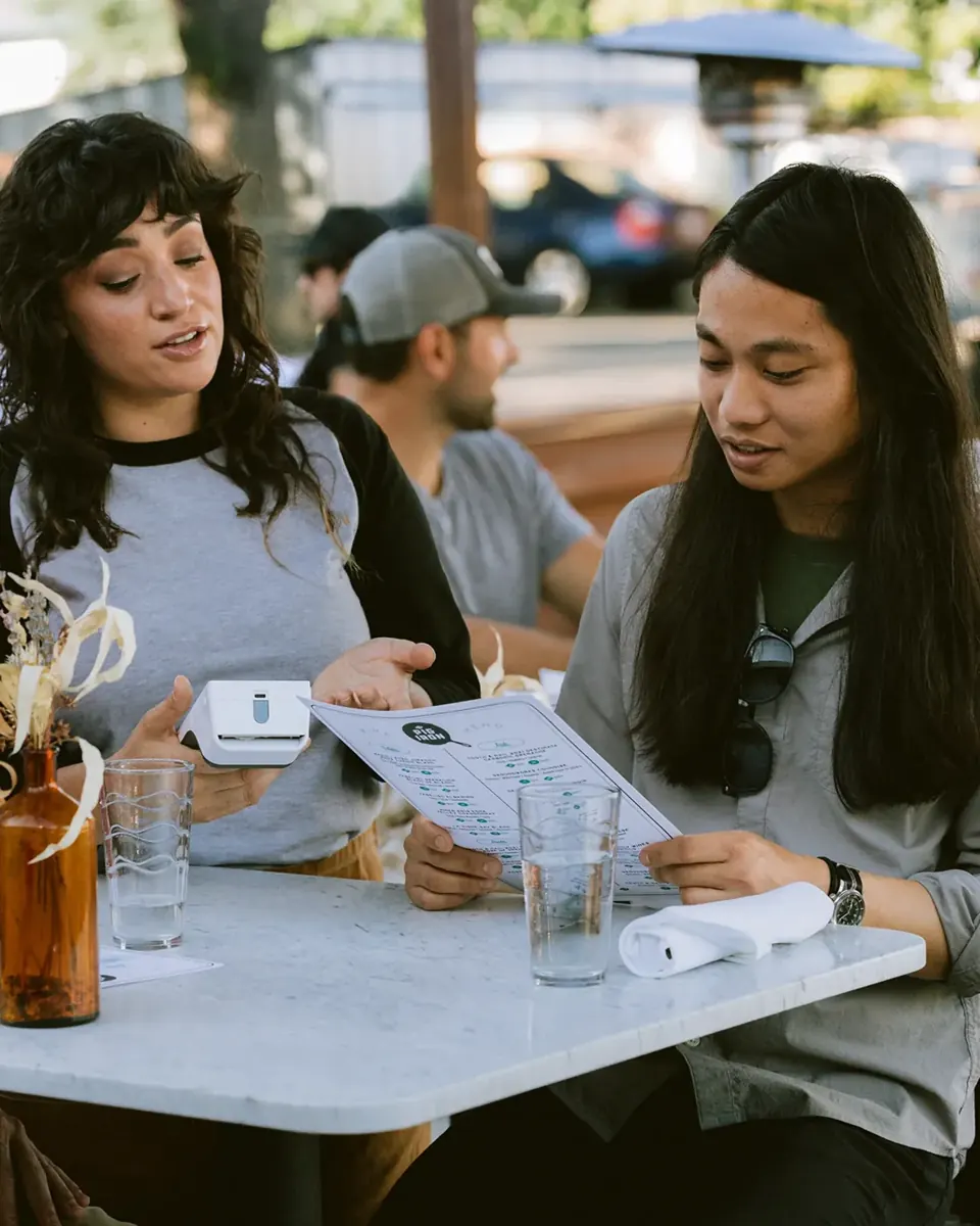 Server taking an order tableside with a handheld payment device