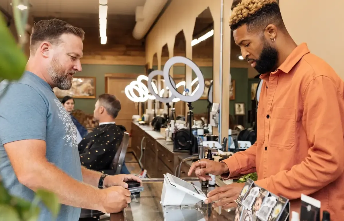 Barbershop owner ringing up a client at the chair-side counter